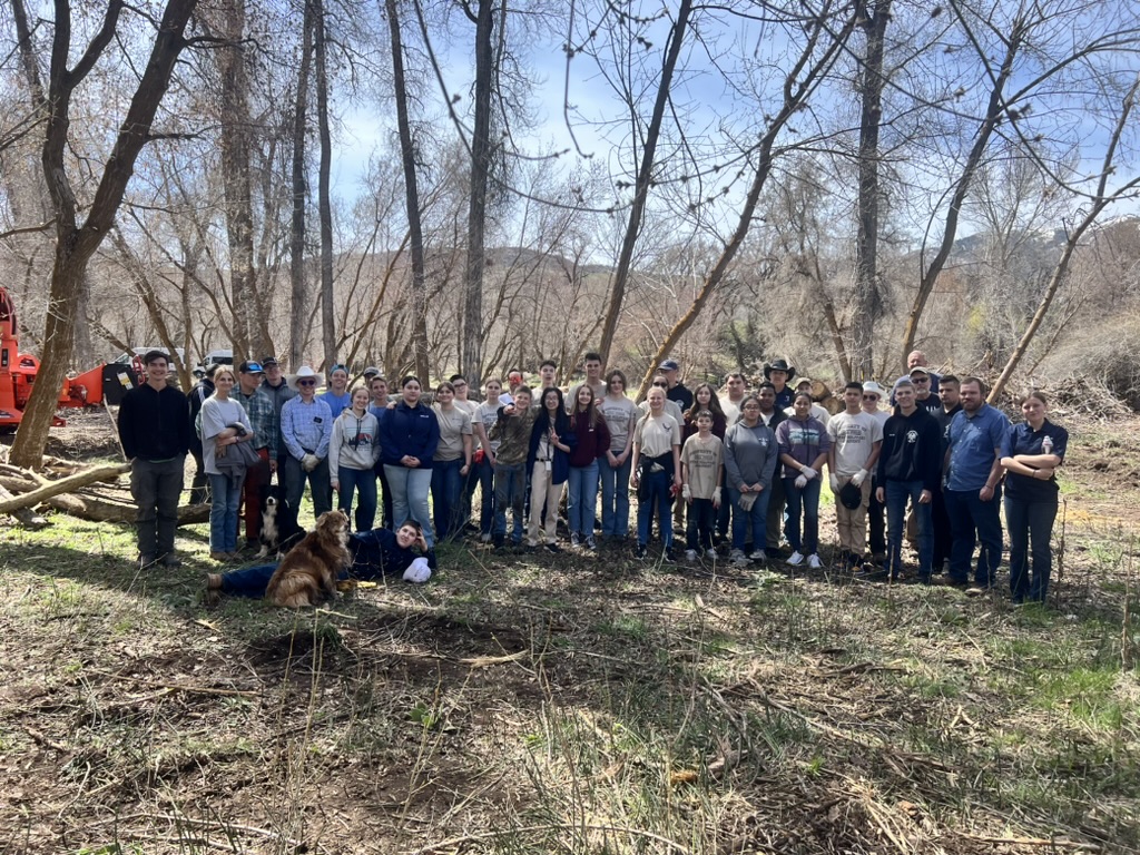 A large group of ranch training participants and mentors gathered together in the woods after a day of work on the ranch.