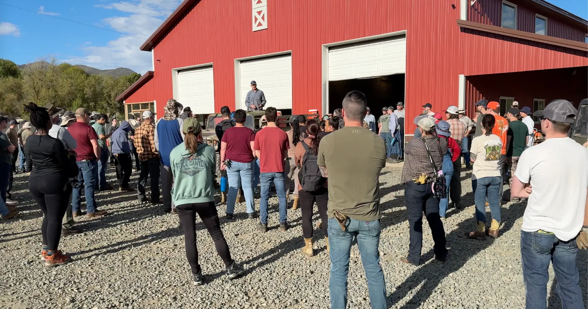A mentor speaks to a large group of ranch participants gathered in front of the red barn.